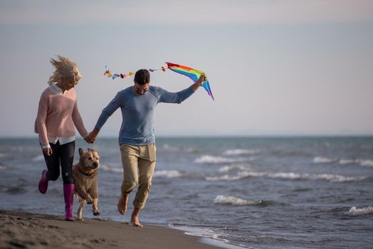 Young Couple having fun playing with a dog and Kite on the beach at autumn day