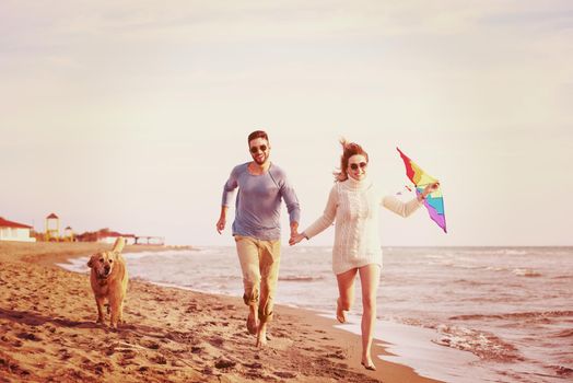 Young Couple having fun playing with a dog and Kite on the beach at autumn day filter