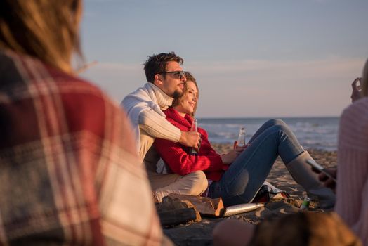 Young Couple enjoying with friends Around Campfire on The Beach At sunset drinking beer