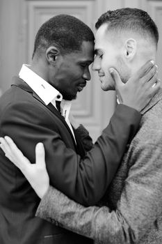 Black and white photo of caucasian man hugging afro american guy, wearing suit. Concept of relationship and same sex couple.