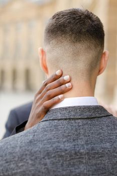 Back view photo of cacuasian boy with black skin hand on neck. Concept of afroamerican man hugging european guy.