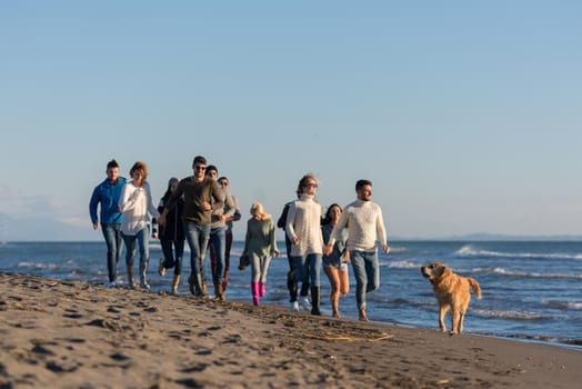 group of young friends spending day together running on the beach during autumn day