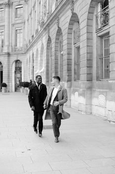 Black and white photo of caucasian man running with afroamerican male person and holding hands in city. Concept of happy gays and strolling.