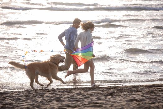 Young Couple having fun playing with a dog and Kite on the beach at autumn day