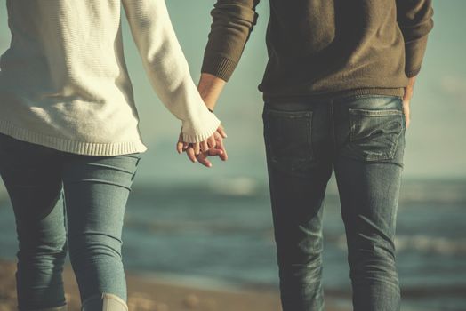 Young couple having fun walking and hugging on beach during autumn sunny day