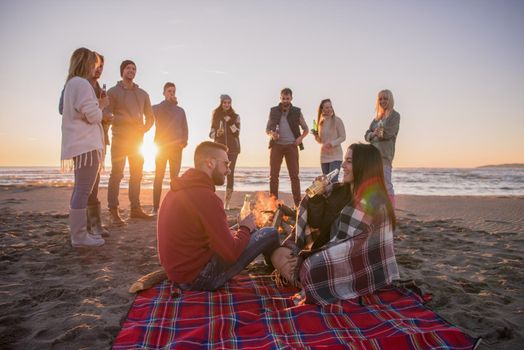 Young Couple enjoying with friends Around Campfire on The Beach At sunset drinking beer