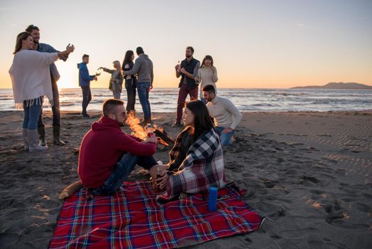 Young Couple enjoying with friends Around Campfire on The Beach At sunset drinking beer