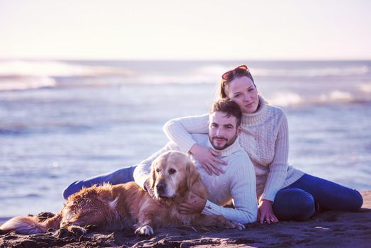 Couple With A Dog enjoying time  together On The Beach at autumn day