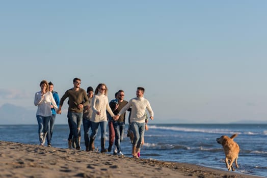 group of young friends spending day together running on the beach during autumn day