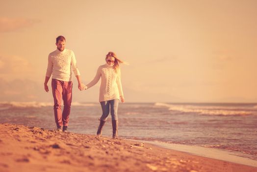 Young couple having fun walking and hugging on beach during autumn sunny day