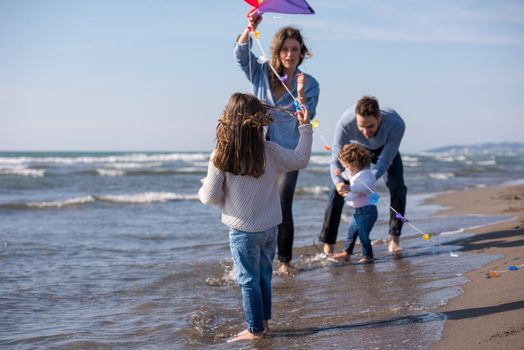 young family with kids resting and having fun with a kite at beach during autumn day