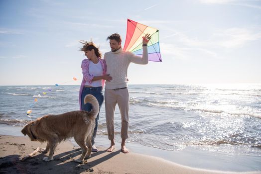 Young Couple having fun playing with a dog and Kite on the beach at autumn day