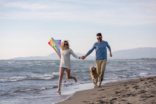 Young Couple having fun playing with a dog and Kite on the beach at autumn day