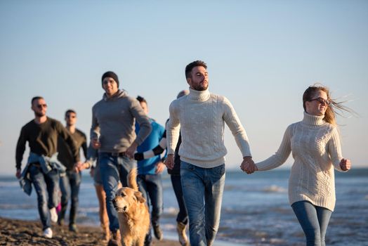 group of young friends spending day together running on the beach during autumn day