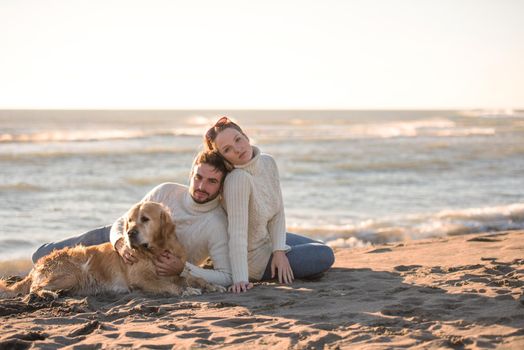 Couple With A Dog enjoying time  together On The Beach at autumn day