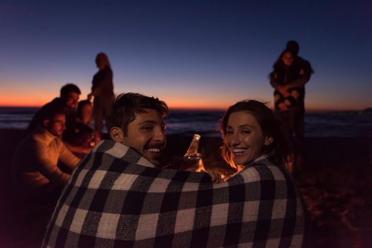 Young Couple enjoying with friends Around Campfire on The Beach At sunset drinking beer