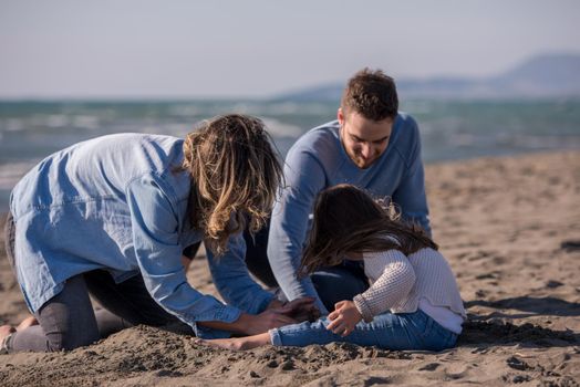 Family with kids resting and having fun at beach during autumn day