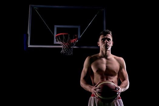 Basketball player portrait  on basketball court holding ball with black isolated background