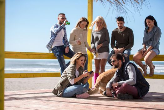 Happy Group Of Friends Hanging Out At Beach House having fun and drinking beer on autumn day