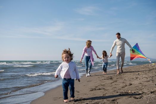 young family with kids resting and having fun with a kite at beach during autumn day