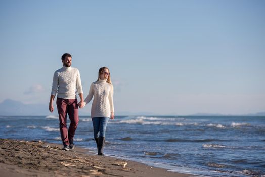 Young couple having fun walking and hugging on beach during autumn sunny day