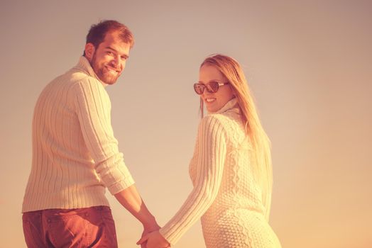 Young couple having fun walking and hugging on beach during autumn sunny day