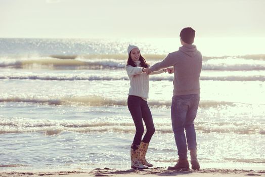 Young couple having fun walking and hugging on beach during autumn sunny day