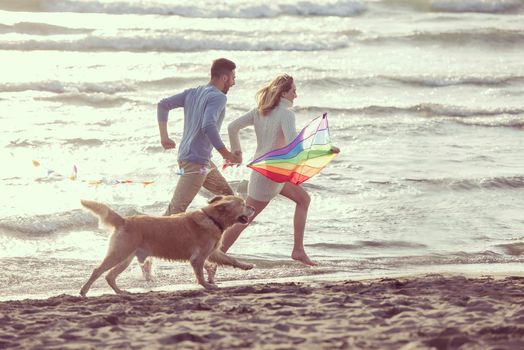 Young Couple having fun playing with a dog and Kite on the beach at autumn day filter