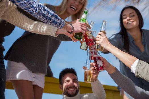 Happy Group Of Friends Hanging Out At Beach House having fun and drinking beer on autumn day