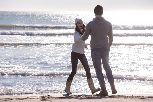 Young couple having fun walking and hugging on beach during autumn sunny day