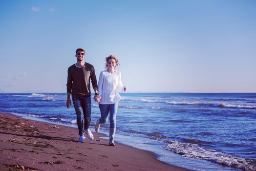 Young couple having fun walking and hugging on beach during autumn sunny day