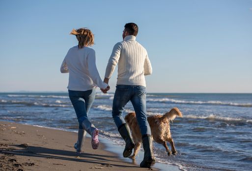 Couple Running On The Beach Holding Their Hands with dog On autmun day