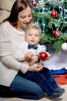 A young mother with a small son near the fireplace and the Christmas tree on the eve of the holidays. The concept of a happy family.