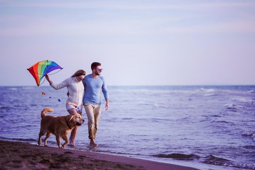 Young Couple having fun playing with a dog and Kite on the beach at autumn day filter