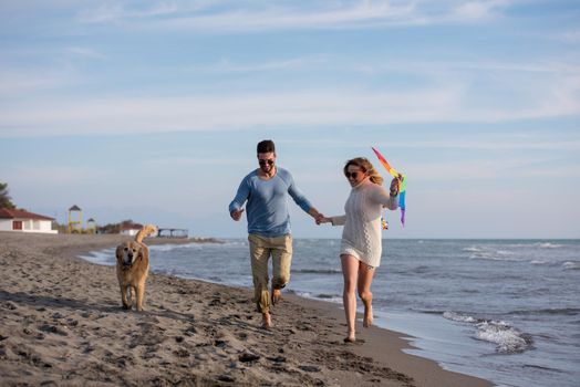 Young Couple having fun playing with a dog and Kite on the beach at autumn day