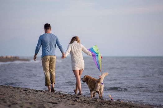 Young Couple having fun playing with a dog and Kite on the beach at autumn day