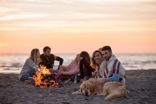 Young Couple enjoying with friends Around Campfire on The Beach At sunset drinking beer