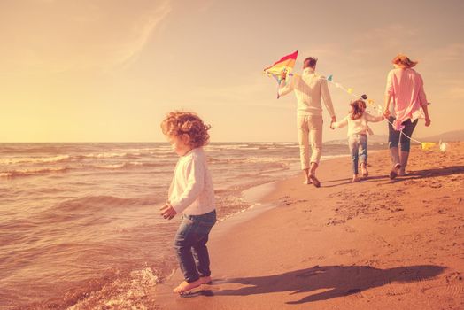 young family with kids resting and having fun with a kite at beach during autumn day filter