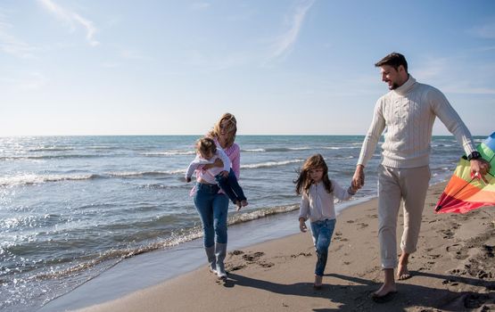 young family with kids resting and having fun with a kite at beach during autumn day