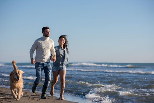 Couple Running On The Beach Holding Their Hands with dog On autmun day