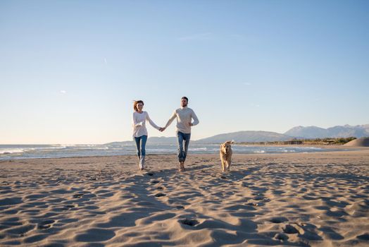 Couple Running On The Beach Holding Their Hands with dog On autmun day