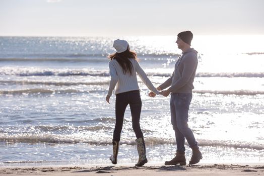 Young couple having fun walking and hugging on beach during autumn sunny day