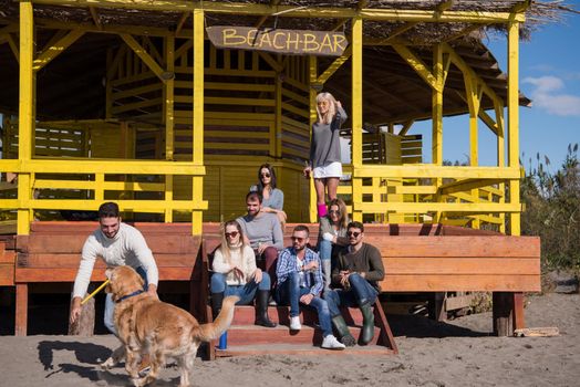 Happy Group Of Friends Hanging Out At Beach House having fun and drinking beer on autumn day