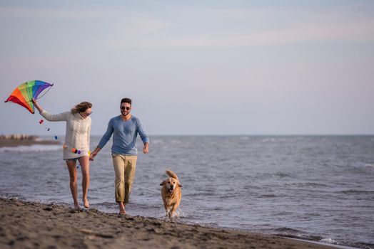 Young Couple having fun playing with a dog and Kite on the beach at autumn day