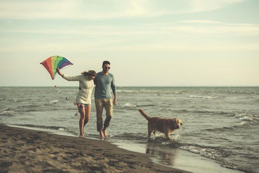 Young Couple having fun playing with a dog and Kite on the beach at autumn day filter