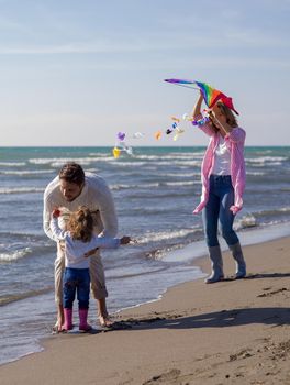 Family with little daughter resting and having fun with a kite at beach during autumn day