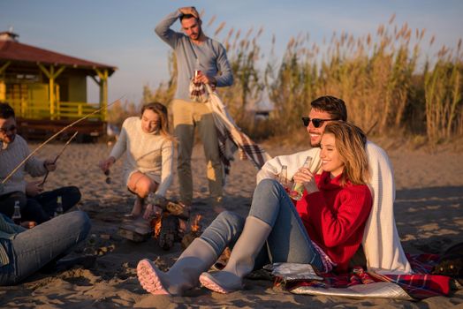 Young Couple enjoying with friends Around Campfire on The Beach At sunset drinking beer