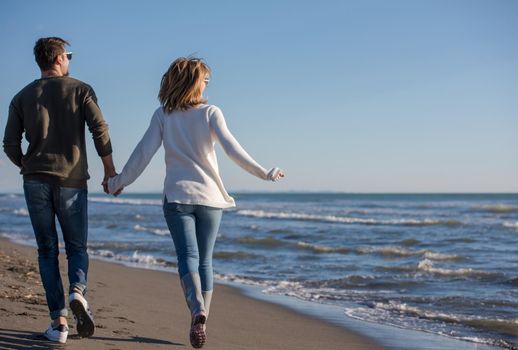 Young couple having fun walking and hugging on beach during autumn sunny day