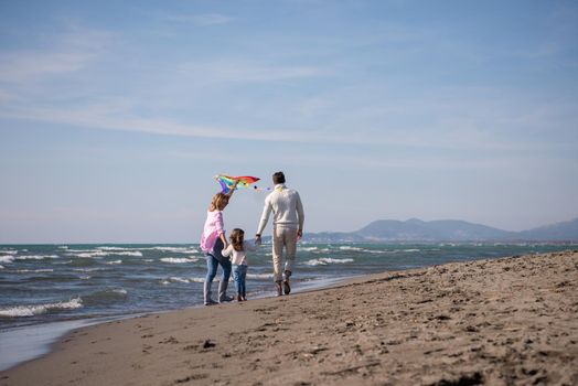 young family with kids resting and having fun with a kite at beach during autumn day