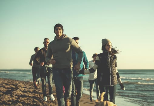 group of young friends spending day together running on the beach during autumn day